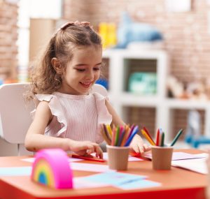 adorable caucasian girl sitting on table drawing on paper at classroom adorable caucasian girl sitting on table drawing on paper at classroom